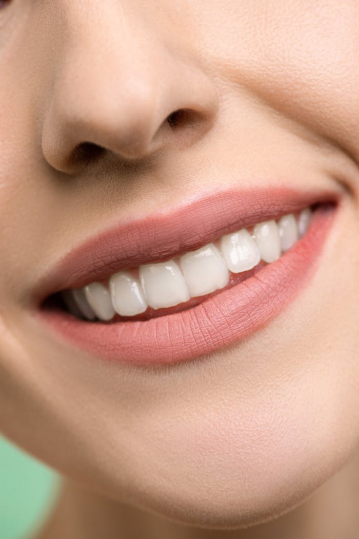 A close-up image focusing on a woman's smiling mouth, showing white teeth and pink lips.