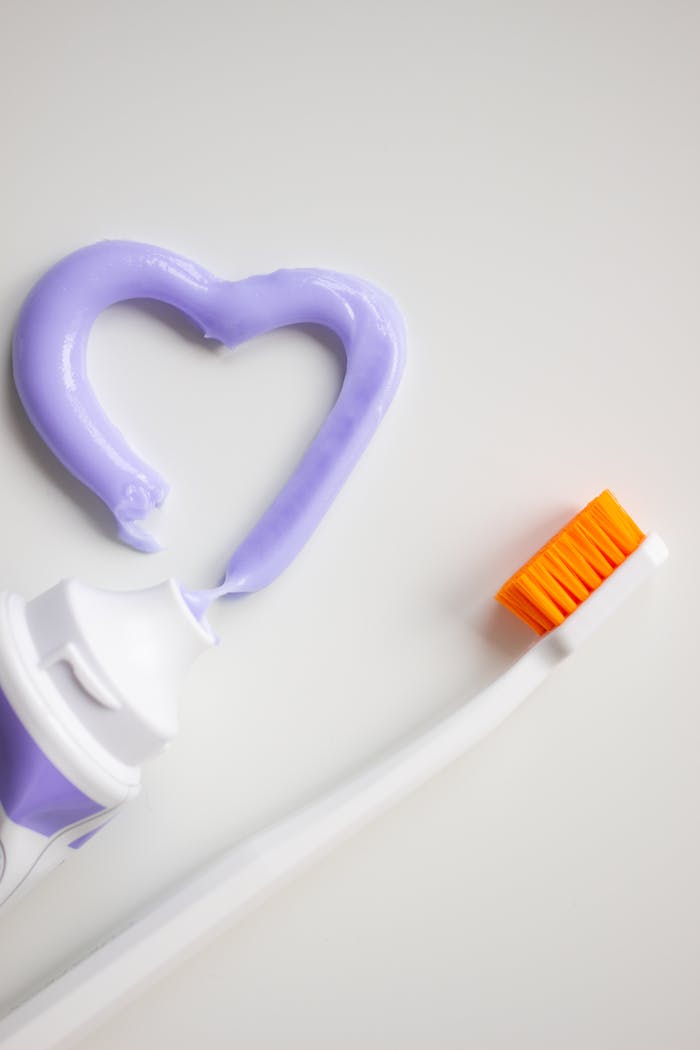Close-up of a toothbrush and purple toothpaste forming a heart shape on a white background.